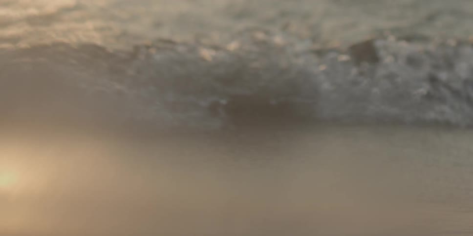 Water splashes up on a sandy beach at sunset