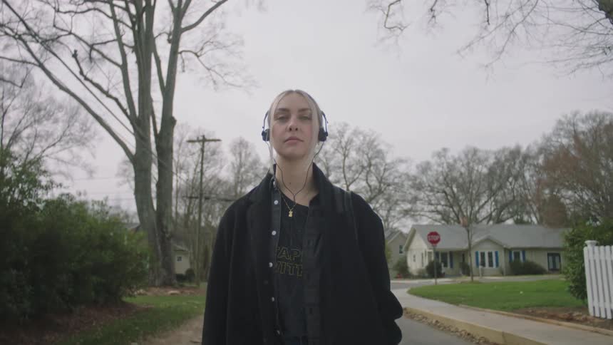 A woman walking through the streets of a neighborhood listening to music on headphones