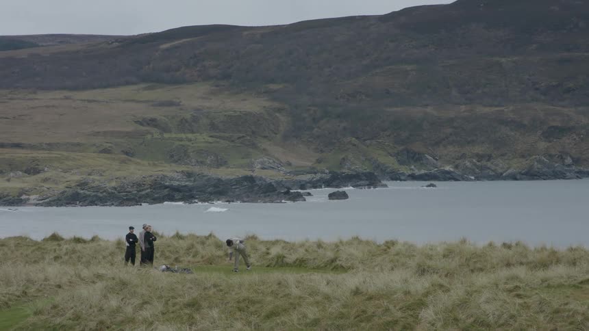 Four men on a seaside golf course with one of them taking a swing