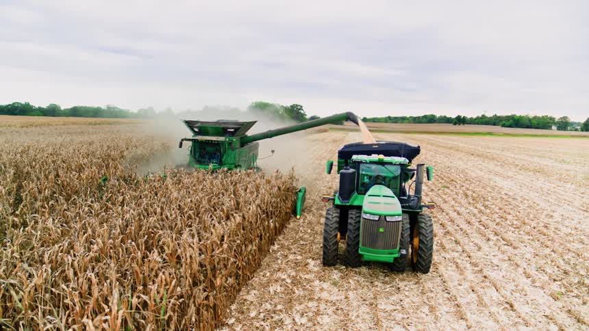 Industrial farm machinery harvesting and dispensing grains at harvest time mid day in the middle America