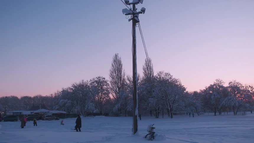 View of a snowcovered park with people walking on a purple morning sky