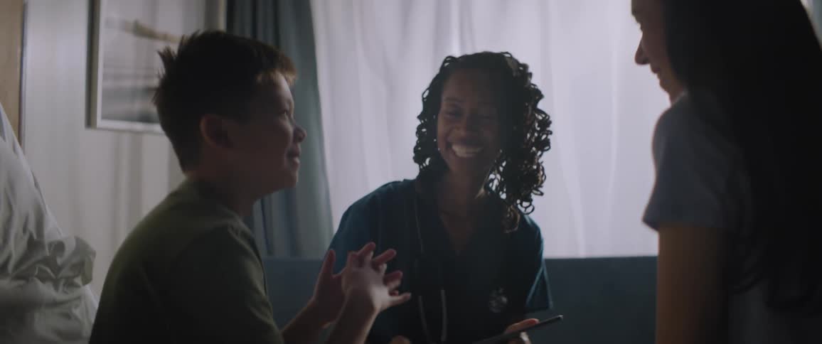 A clip of a kid and two nurses having a conversation on the bed