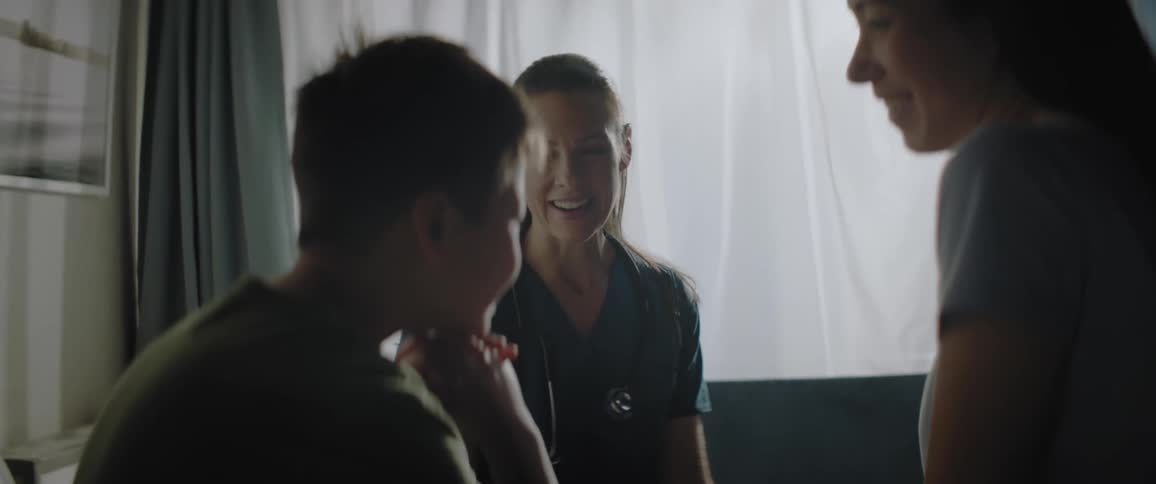 Mother talking to her son sitting on a hospital bed in the presence of a nurse and everyone is smiling