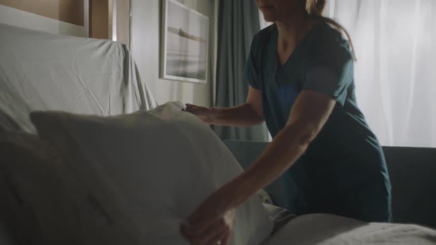 Nurse fluffs pillow on hospital bed
