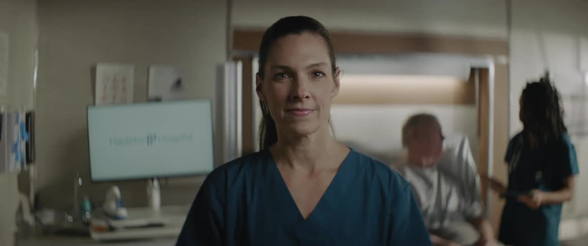 A medical professional smiles while behind her another cares for a patient