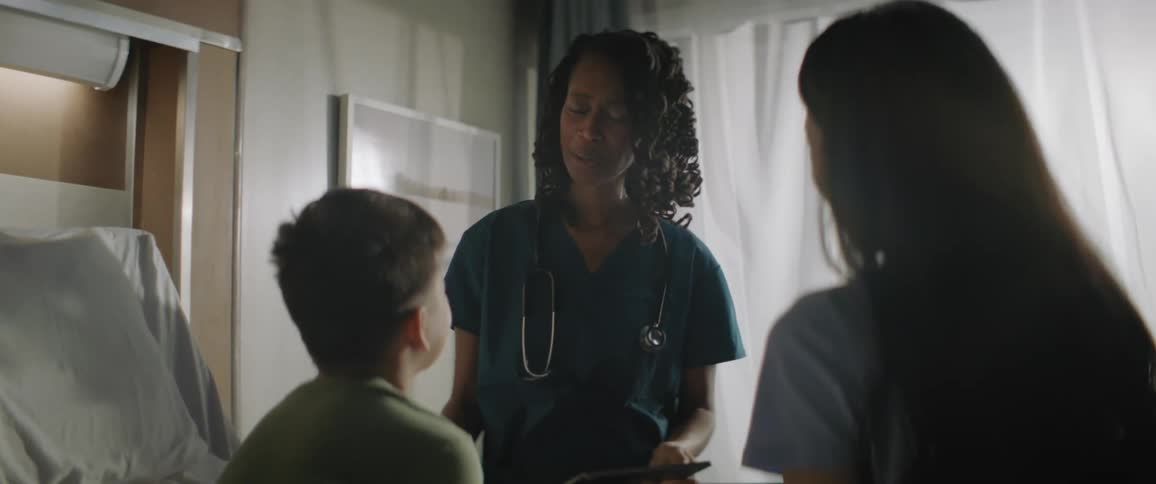 Medical professional wearing scrubs smiles while talking to patient and his mother