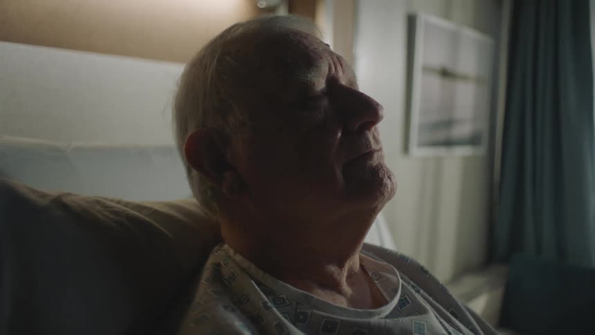 A man in hospital clothes breathing deeply in bed