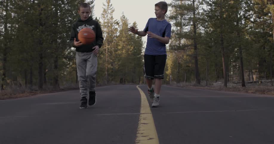 Two boys walk down the street dribbling a basketball