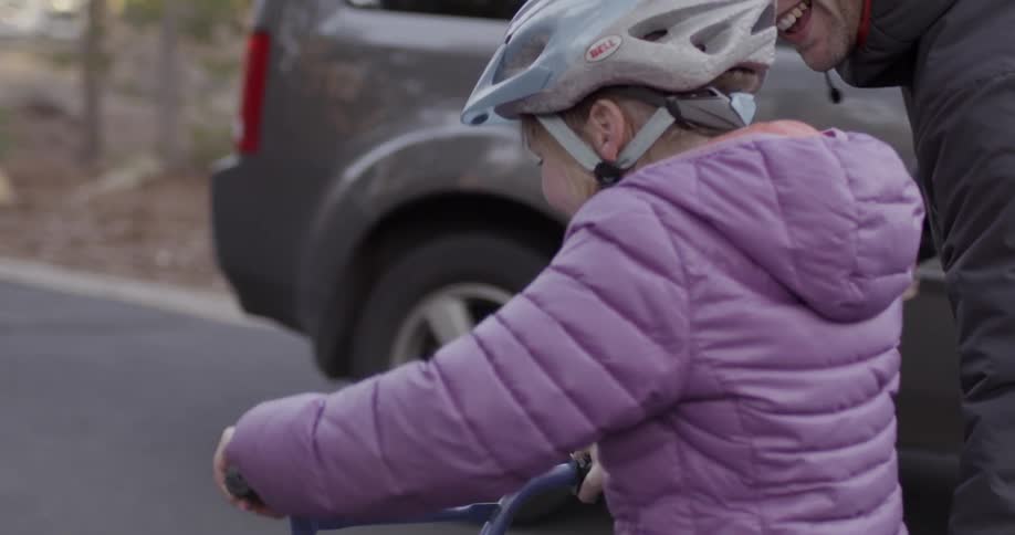 Young girl learning to ride a bike with the help of her father