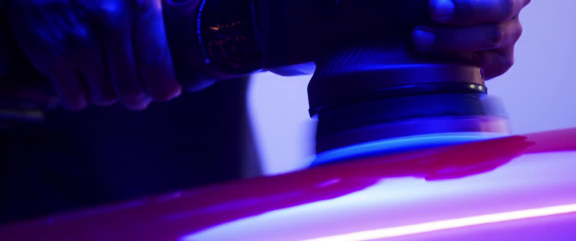 Someone using a machine to polish a red metal surface