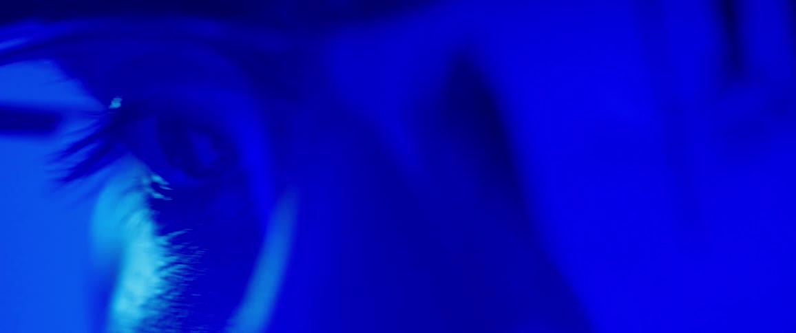 Someone with blue light shining on them and wearing glasses blinks while looking intently at something