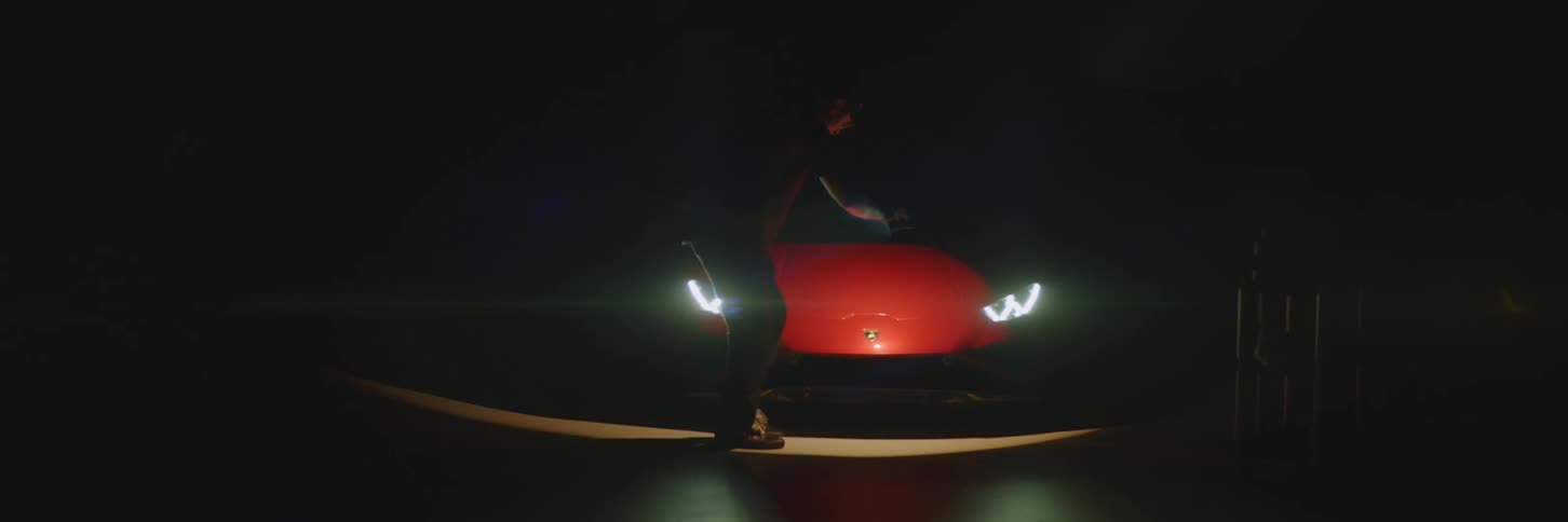 A person walking in front of a red sports car with its headlights on in a dark environment