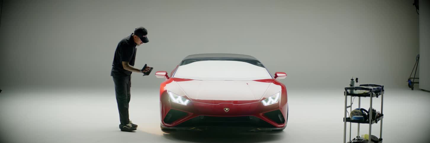 Man with a flashlight inspecting a red lamborghini inside a studio