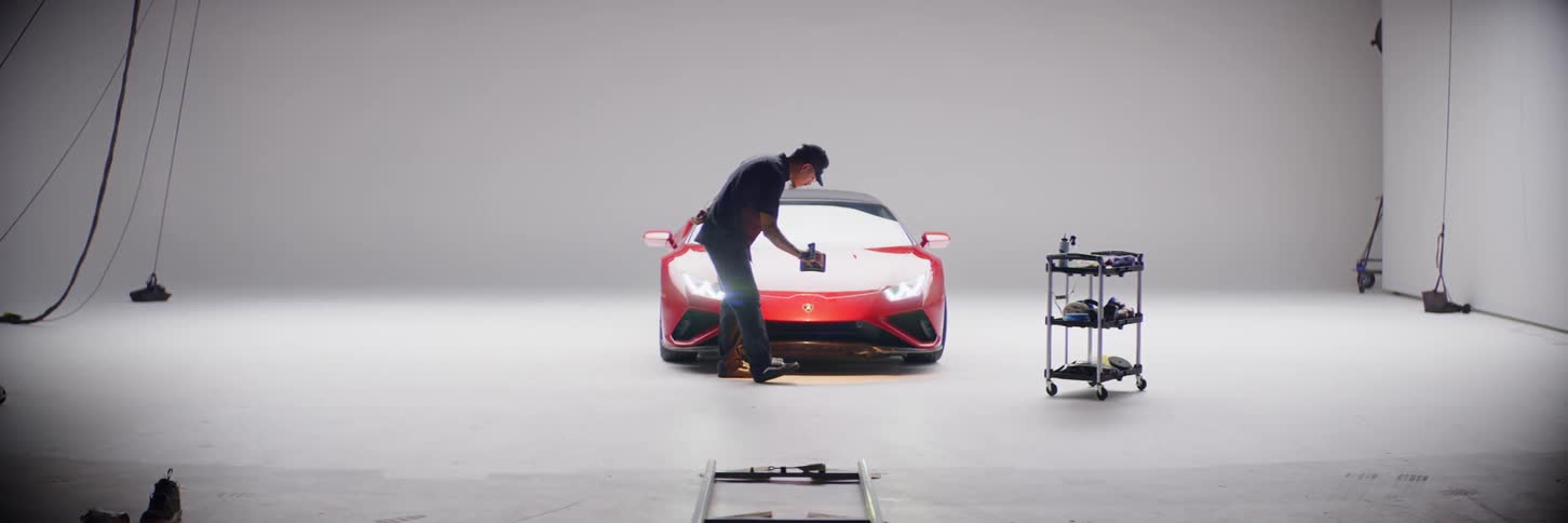 A man slowly running a lamp over the hood of a red luxury car