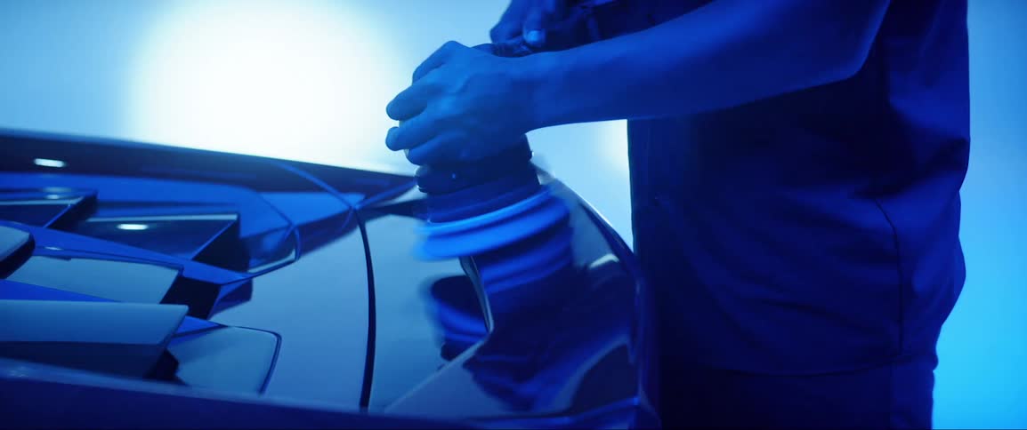 A man using a machine to polish the back of a luxury car