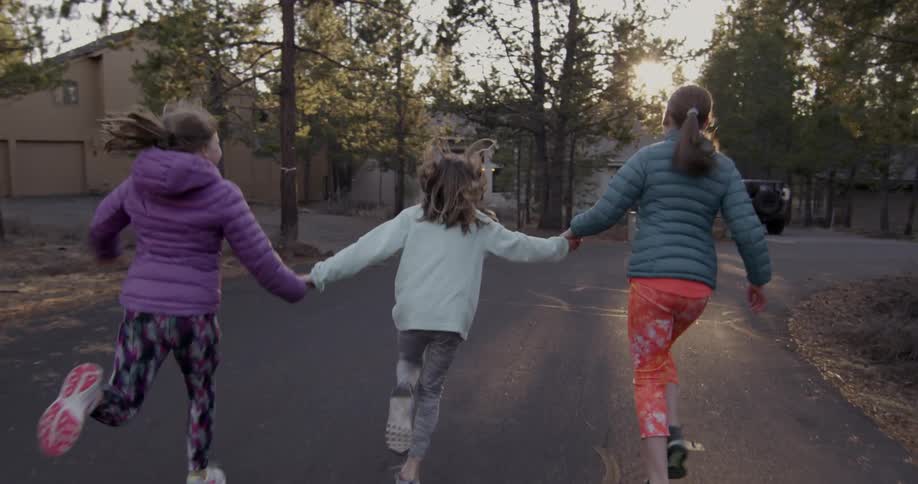 Three children hold hands running on the road