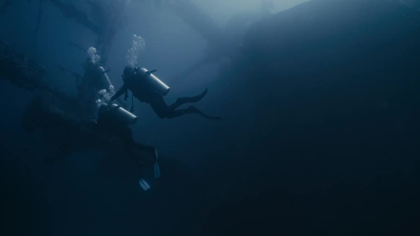 Divers at the bottom of the ocean observing a sunken ship