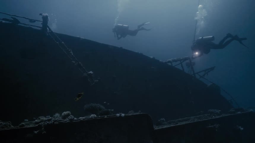 Two divers at the bottom of the sea amidst a wreckage of a vessel