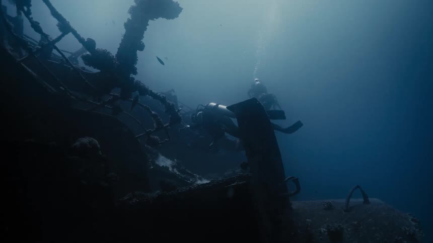 Two divers with equipment are underwater next to a sunken ship