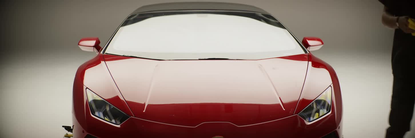 Man wiping the hood of a red lamborghini inside a studio