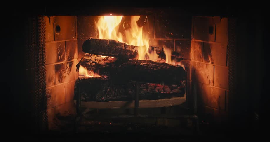 A fire burns in an indoor fireplace with logs on a metal andiron