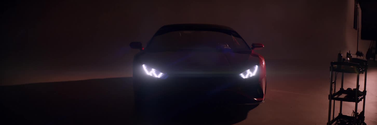 Dark room with a red lamborghini with headlights on followed by lights turning on inside a studio
