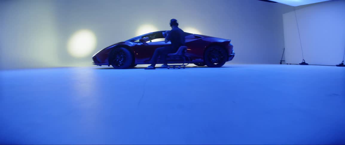 A man in a rolling chair pushes away from a very sleek sports car