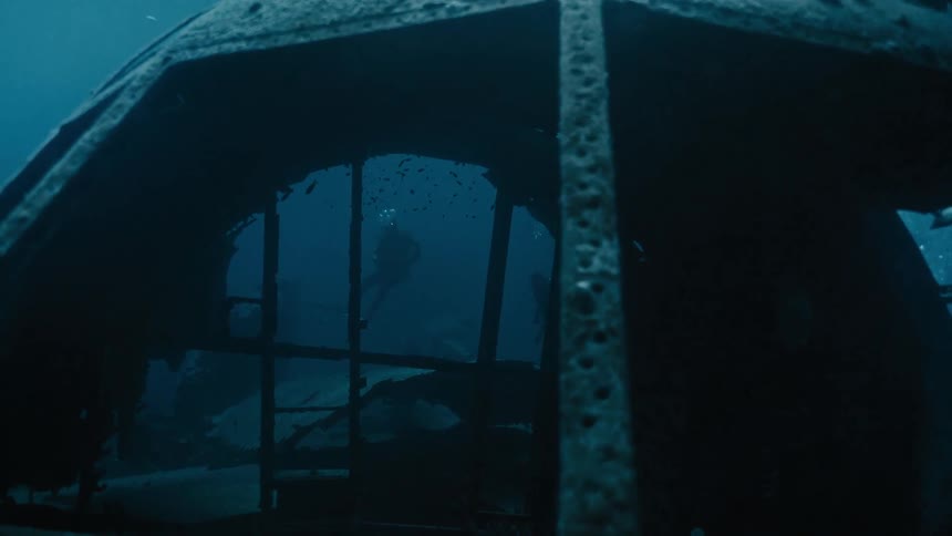 Two people in diver suit scuba diving under the ocean near a shpwreck