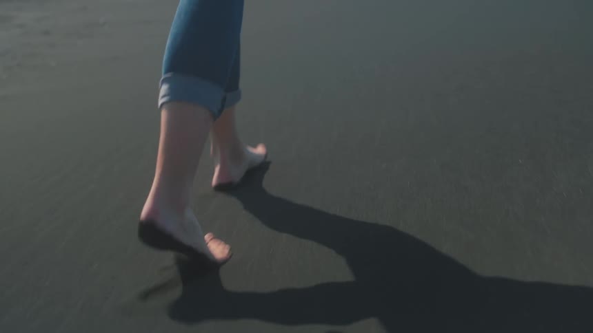 Closeup on the feet of a woman walking amidst black sand