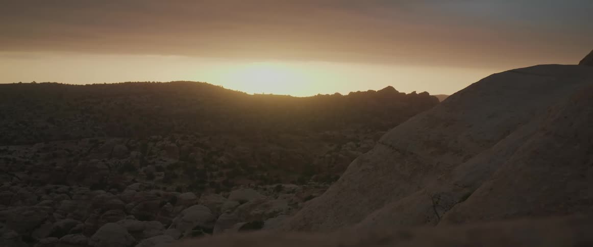 A view of a region with rocks on the ground and the sun rising on the horizon in the morning