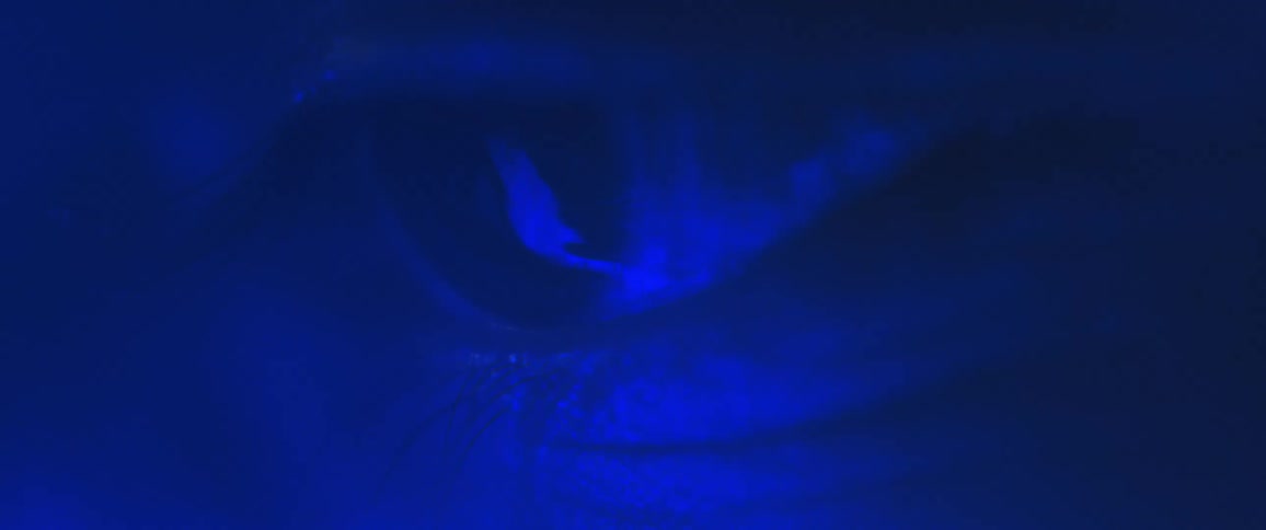 Extreme closeup of a mans eye blinking with blue lights shining beneath