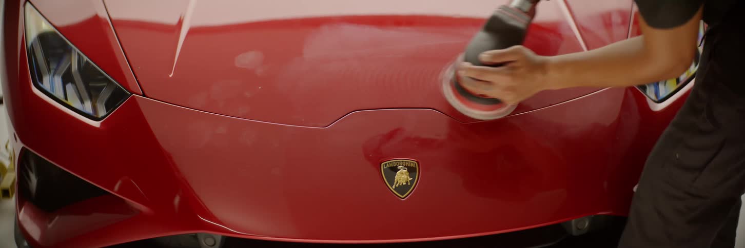 A person polishing the front of a luxury car with a power tool