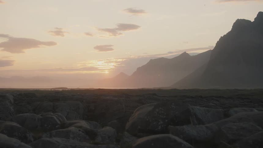 View of rocks by the sea with the mountainous coast to the side and the sunrise on the horizon
