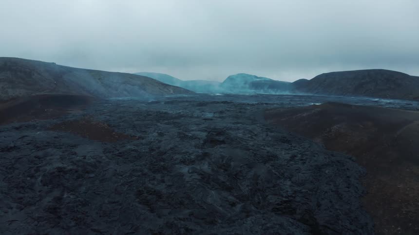 Aerial of a barren volcanic mountain peak with steam flowing up into a hazy sky