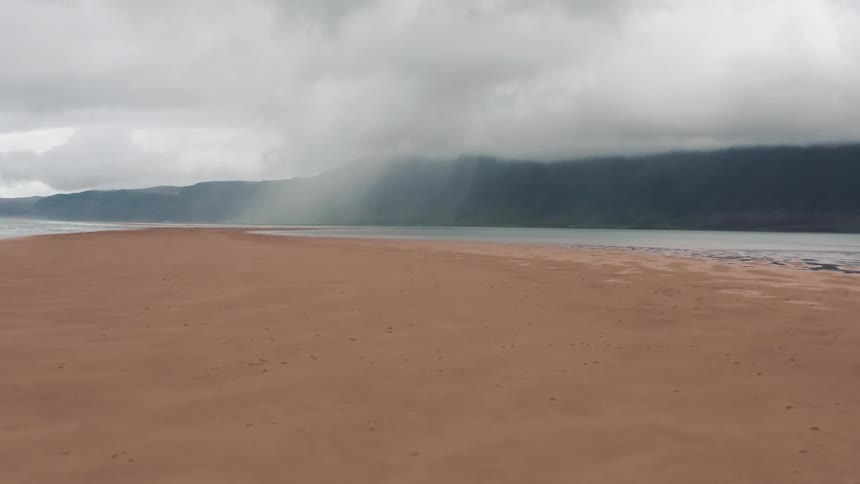 Panorama of a sandy riverbank with a mountain range on a cloudy day