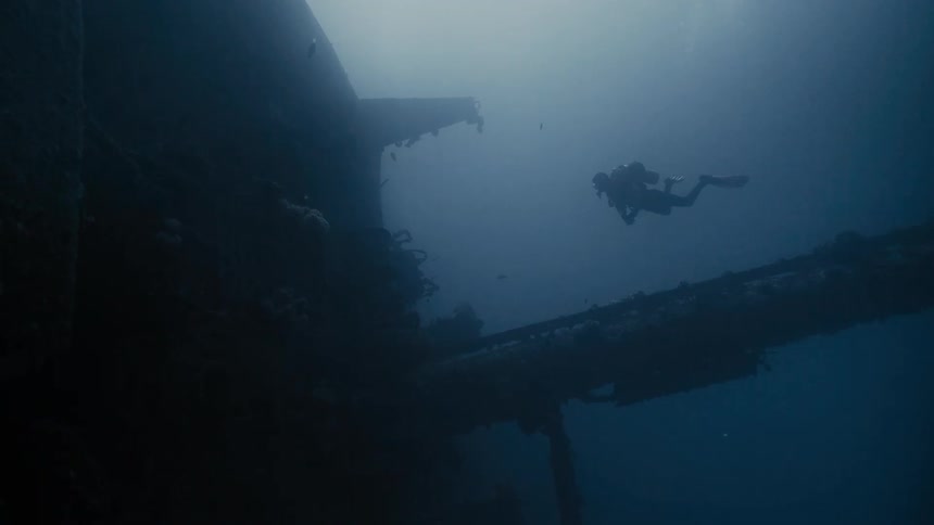 Scuba diver swimming next to mast of a wrecked ship in the ocean with sunlight brightening the water above