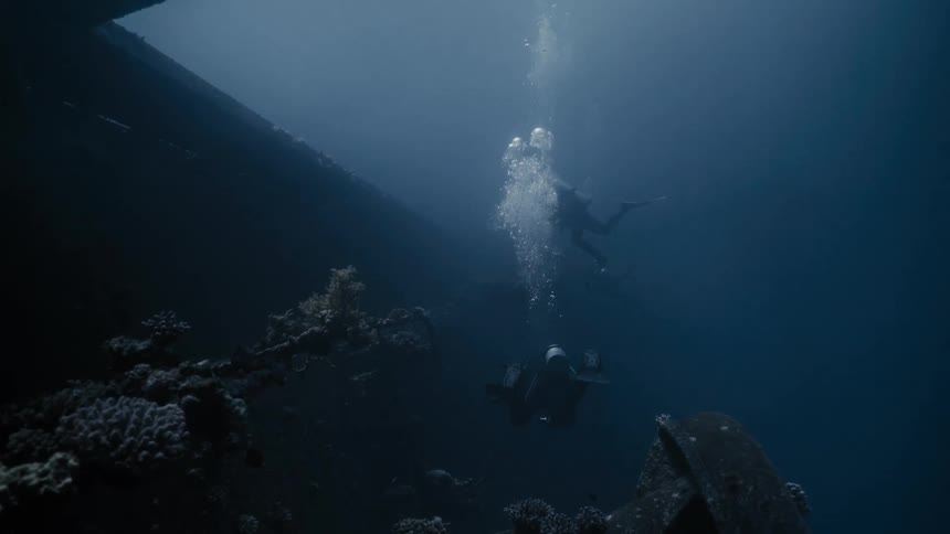 A pair of scuba divers explore a shipwreck on the ocean floor