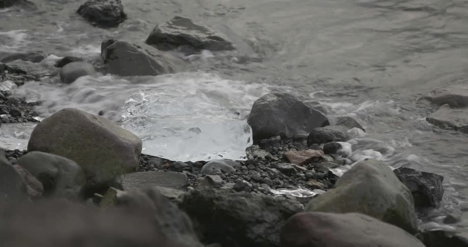 Ice rest on the rocky shore as waves crash onshore