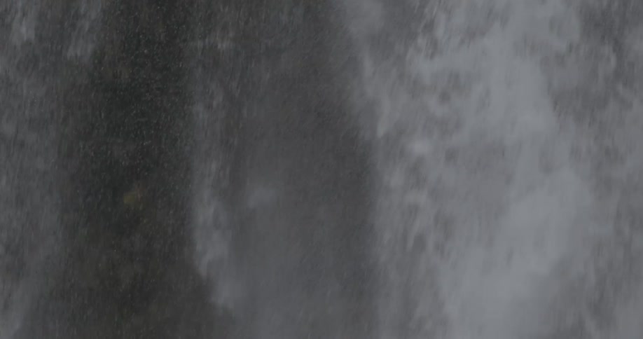 A tall waterfall drops water down spraying all over