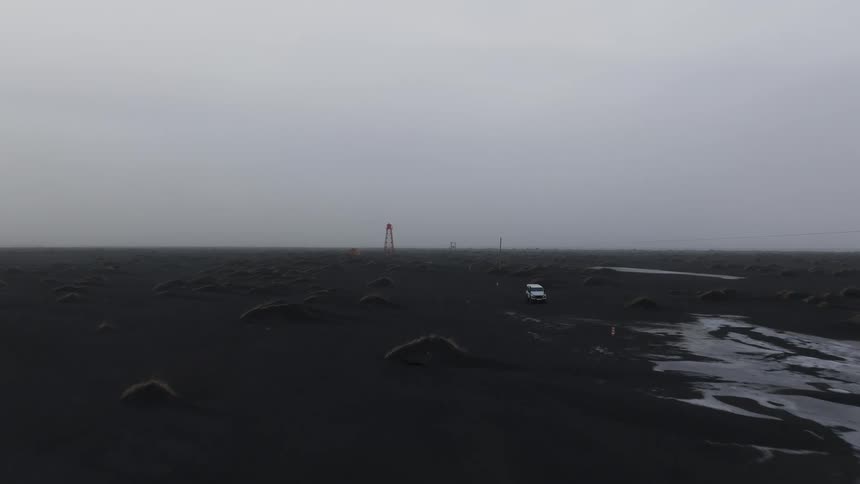 A region with black soil and a white car passing by and behind it there is a small towershaped building