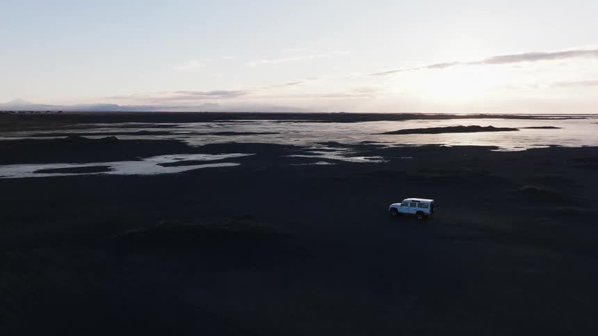 Aerial panorama of a vehicle passing through black soil with a lake on a morning