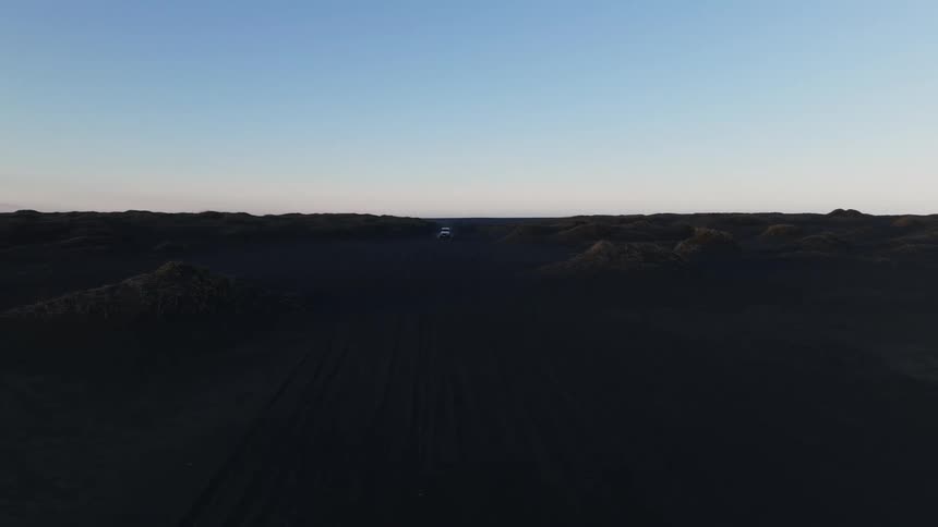 A car driving along a dirt road in the desert during sunrise