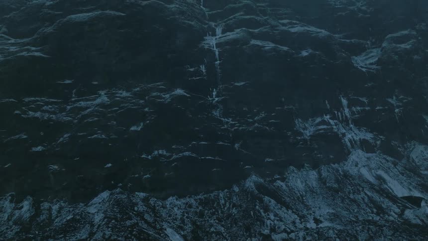 Top view of the foot of a mountain with black soil and frozen patches on a dark day