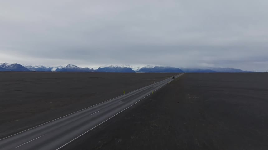A car headed down a deserted road across a plain heading towards a mountain range