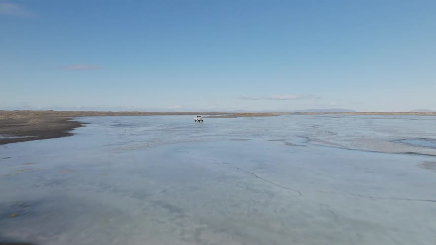 A white jeep drives across a frozen lake