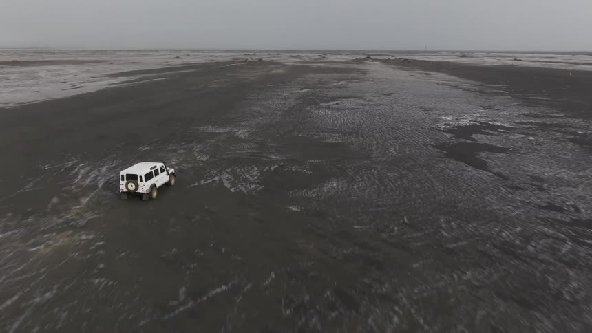 White jeep driving through a natural black soil on a cloudy day