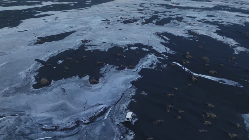 Aerial panorama of a jeep traversing through black soil with frozen patches on a cloudy morning