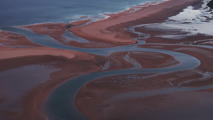 Aerial view of a river gracefully winding through golden sands before merging with the crystalclear azure waters of the ocean