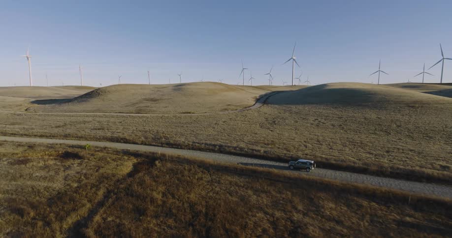 Car driving on a road beside a grassland with wind energy platforms