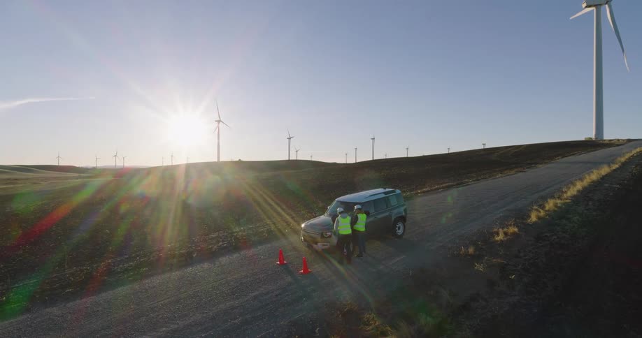 Aerial of engineers stand by green jeep with wind turbines in the background